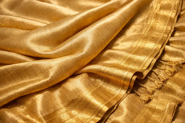 A handwoven Muga silk saree displaying its natural golden sheen under warm light.